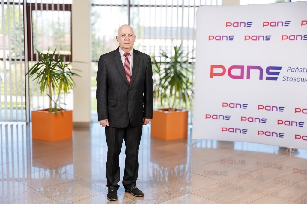 Mężczyzna w garniturze przed logo PANS Państwowej Uczelni Zawodowej