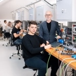 Dwóch mężczyzn pracuje z nowoczesnym sprzętem w sali dydaktycznej, ucząc się automatyki i elektroniki.