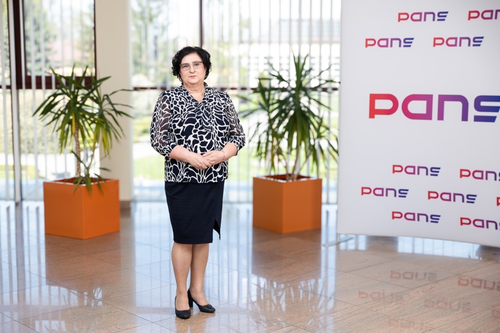 Kobieta w stroju biznesowym stoi przed logo PANS