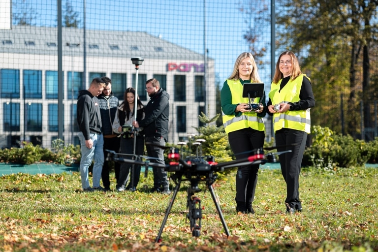 Zespół geodetów z dronem i sprzętem pomiarowym na trawie
