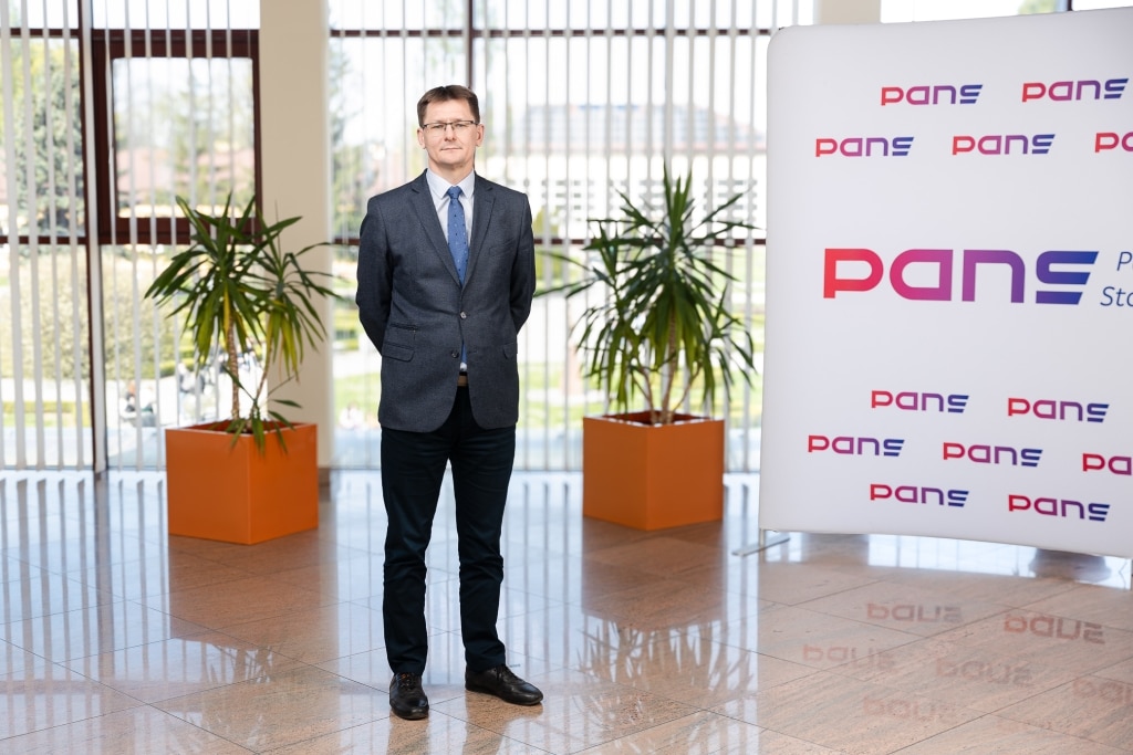 Mężczyzna w garniturze stoi przed logo PANS.