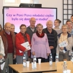 Międzypokoleniowe spotkanie: starsi i młodsi słuchają prelekcji na ekranie.