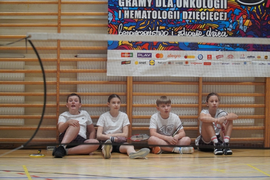 Dzieci siedzą na podłodze przy siatce do badmintona podczas turnieju WOŚP