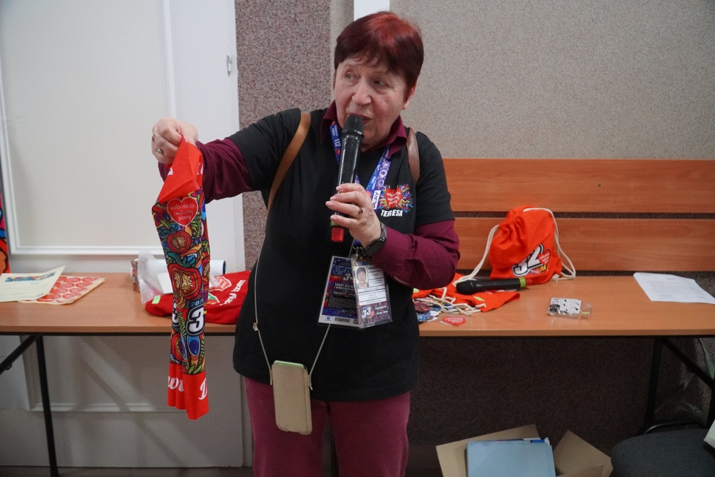 Kobieta z mikrofonem prezentuje czerwony szalik WOŚP na Wydziale Ochrony Zdrowia PANS w Jarosławiu.