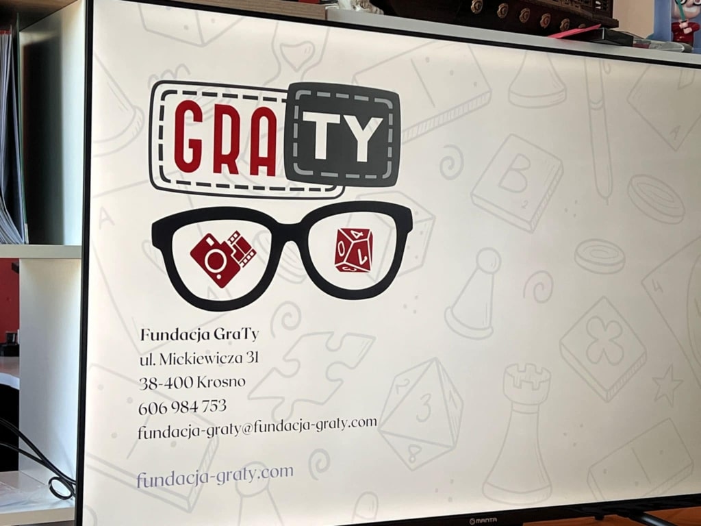 Logo Fundacji GraTy z okularami, elementami gier i danymi kontaktowymi
