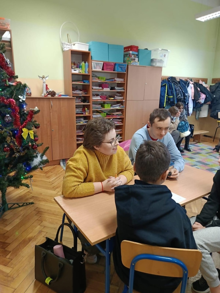 Studenci psychologii odwiedzają uczniów w klasie, rozmowa przy stole.