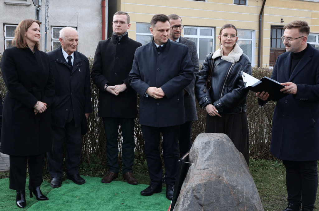 Uczestnicy XXVI sesji Rady Miasta stoją przy kamieniu pamiątkowym.