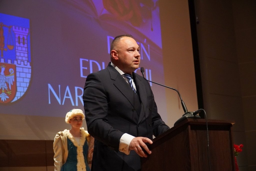 Mężczyzna w garniturze przemawia na tle napisu "EDUKACJA NARODOWA".