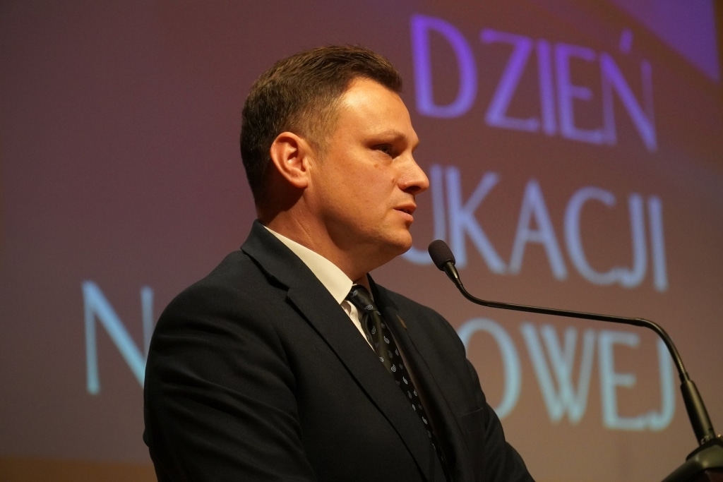 Mężczyzna w garniturze przemawia na tle napisu "Dzień Edukacji Narodowej