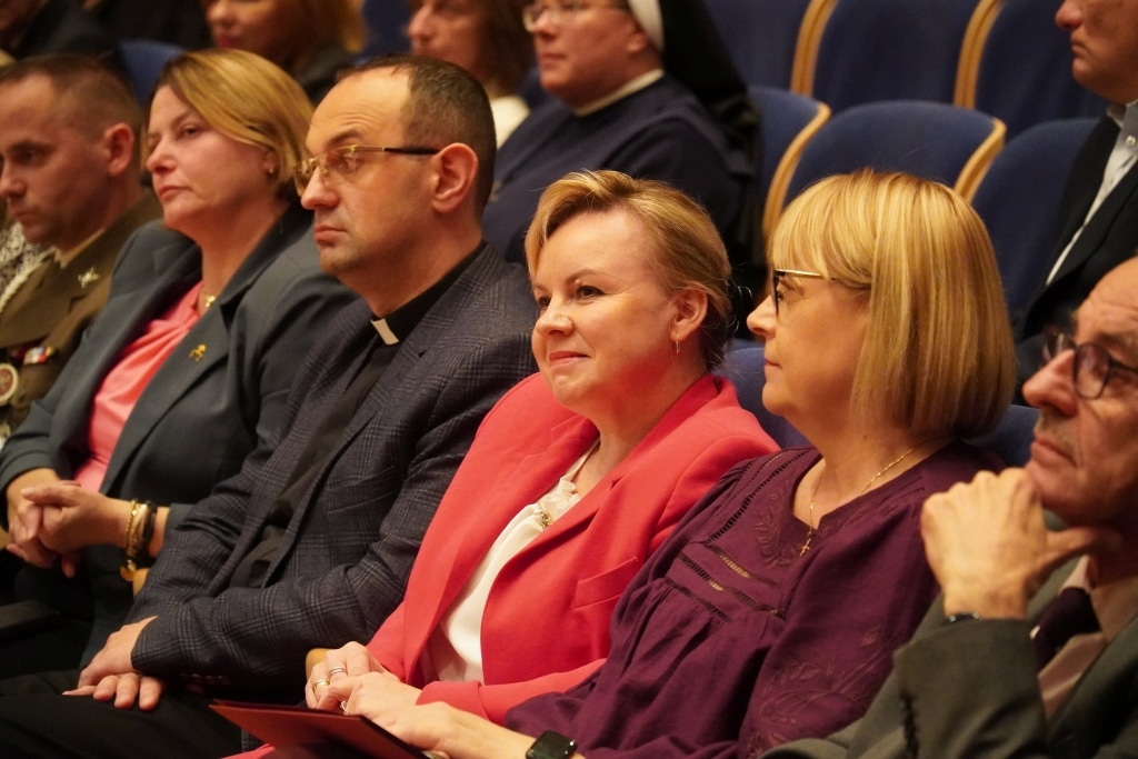 Uczestnicy uroczystości Dnia Edukacji Narodowej siedzą w rzędzie.