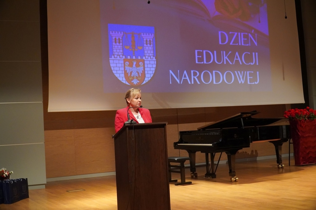 Kobieta przemawia na tle ekranu z napisem „Dzień Edukacji Narodowej”