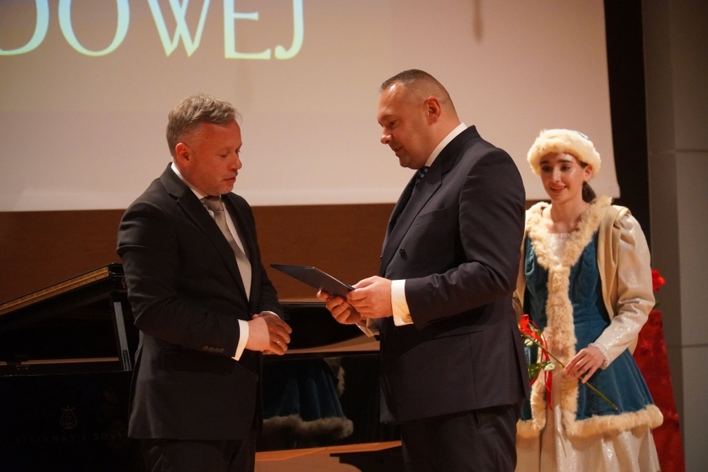 Uroczystość Dnia Edukacji Narodowej: wręczenie dyplomu, mężczyźni w garniturach, dziewczyna w stroju ludowym