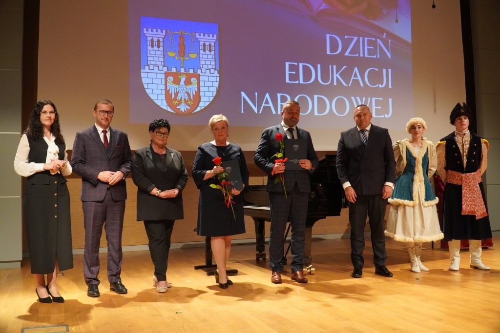Uczestnicy obchodów Dnia Edukacji Narodowej na scenie z logo i hasłem.