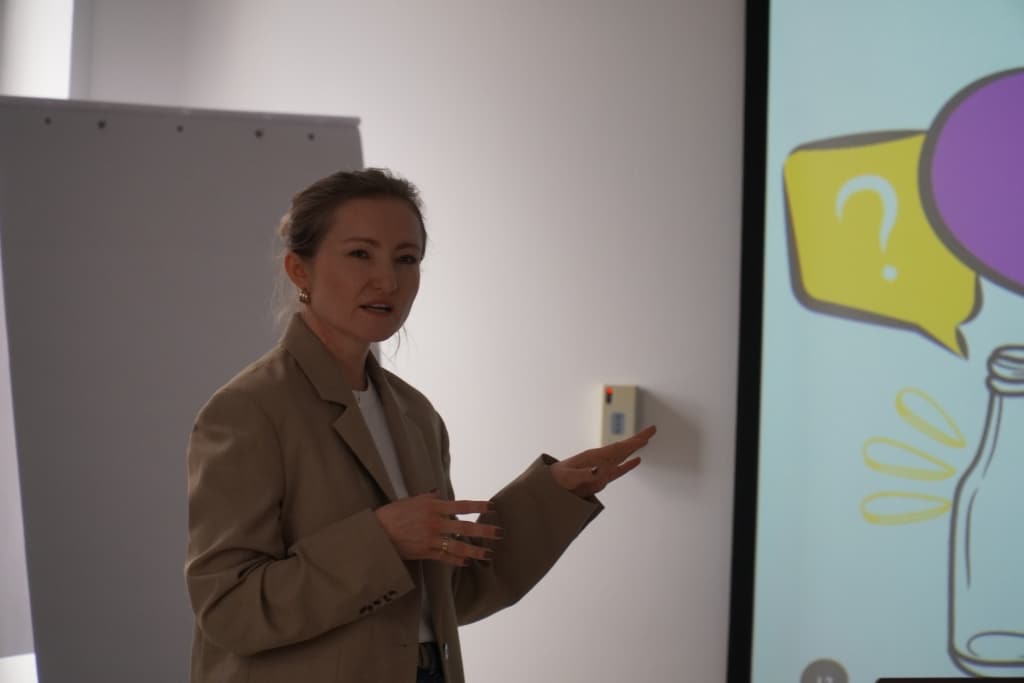 Kobieta w marynarce wygłasza prezentację podczas wizyty studyjnej w Hucie Szkła O-I.