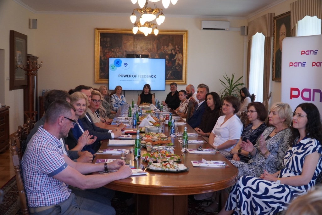 Spotkanie podsumowujące współpracę: ludzie przy stole, ekran z napisem "Power of Feedback
