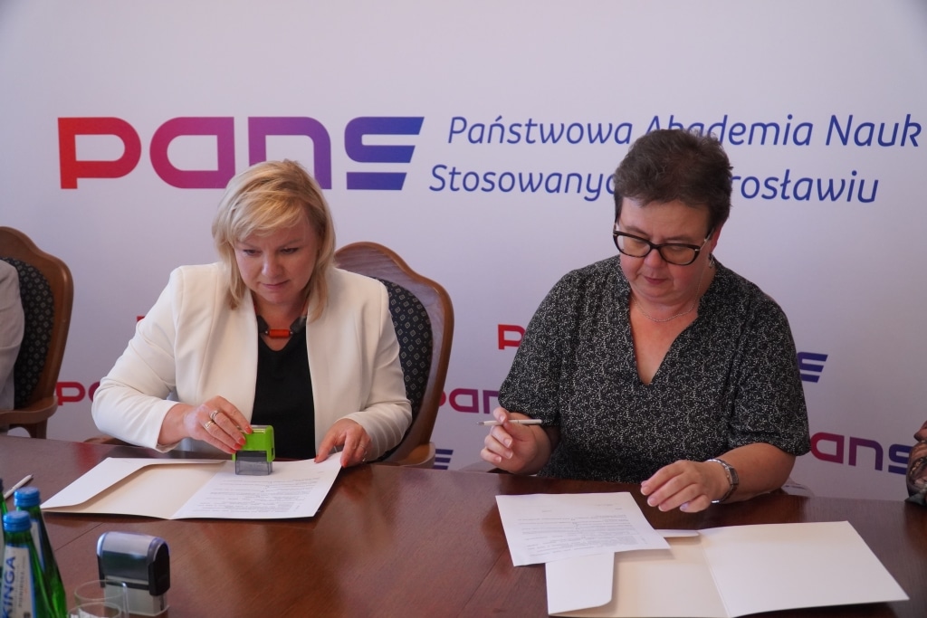 Dwie kobiety podpisują dokumenty na tle logo PANS Jarosław.