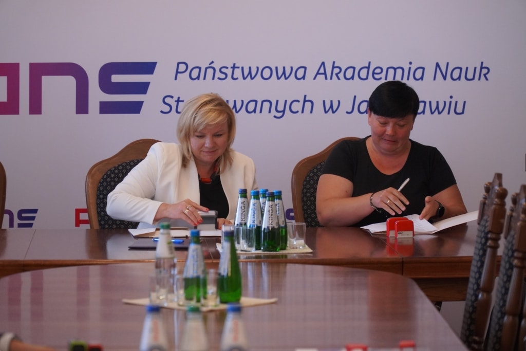 Dwie kobiety podpisują dokumenty na tle logo Państwowej Akademii Nauk w Jarosławiu.