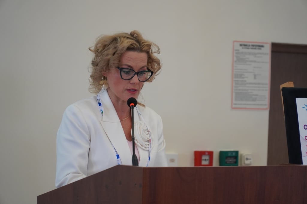 Kobieta w białej marynarce mówi do mikrofonu na konferencji naukowej