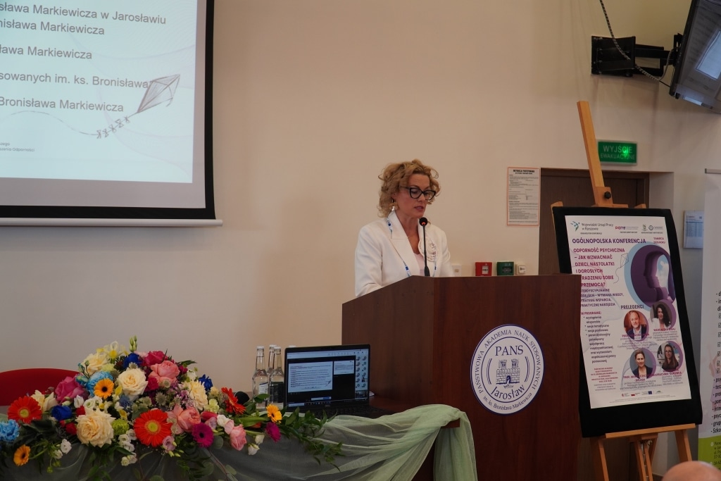 Konferencja naukowa: prelegentka przy mównicy, plakat o odporności psychicznej