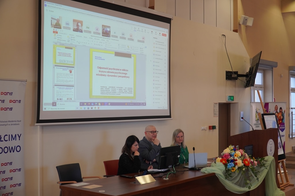 Konferencja naukowa „Odporność psychiczna”: prelegenci przy stole, ekran z prezentacją.