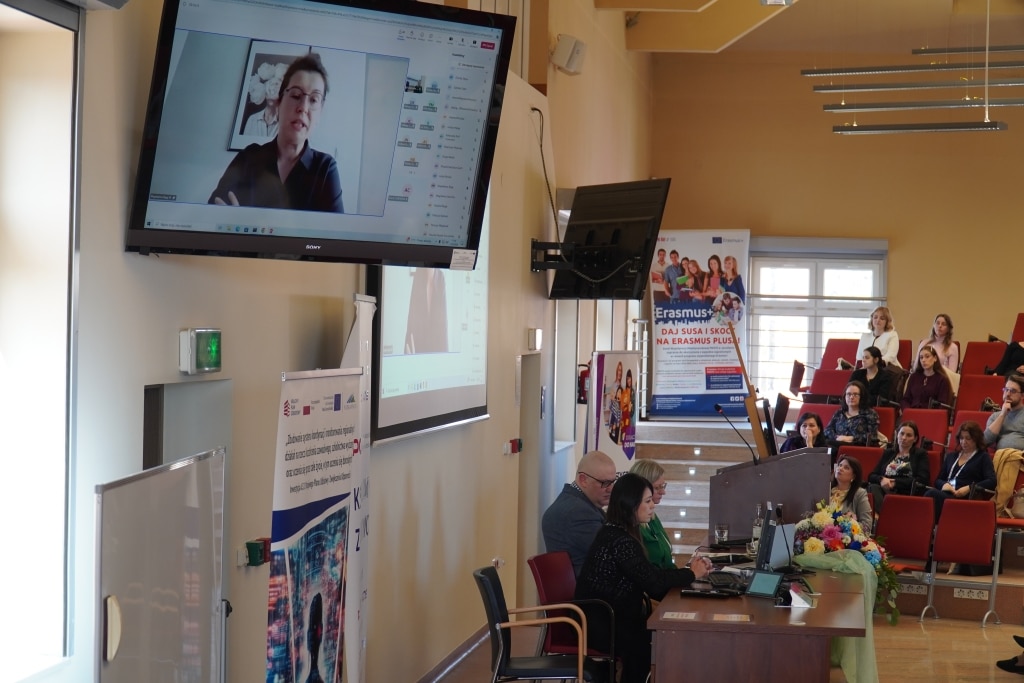 Konferencja naukowa: prelegentka online, uczestnicy na sali, Erasmus+