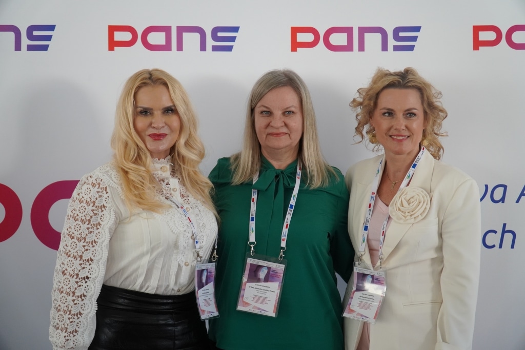 Trzy kobiety na tle logo PANS na konferencji naukowej.