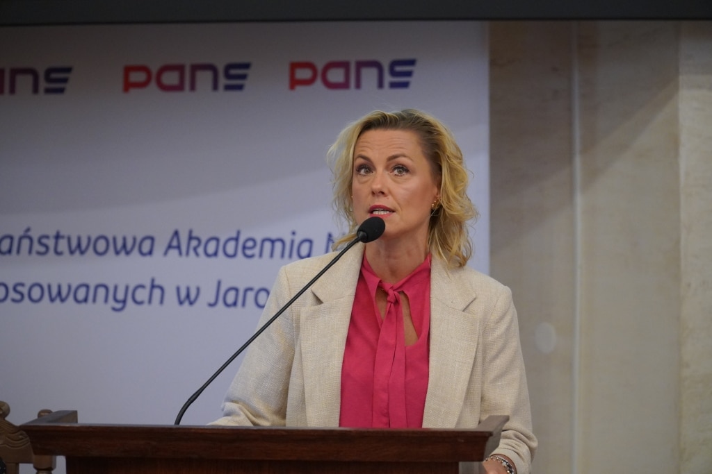 Kobieta w różowej bluzce i beżowej marynarce przemawia przy mównicy na konferencji PANS