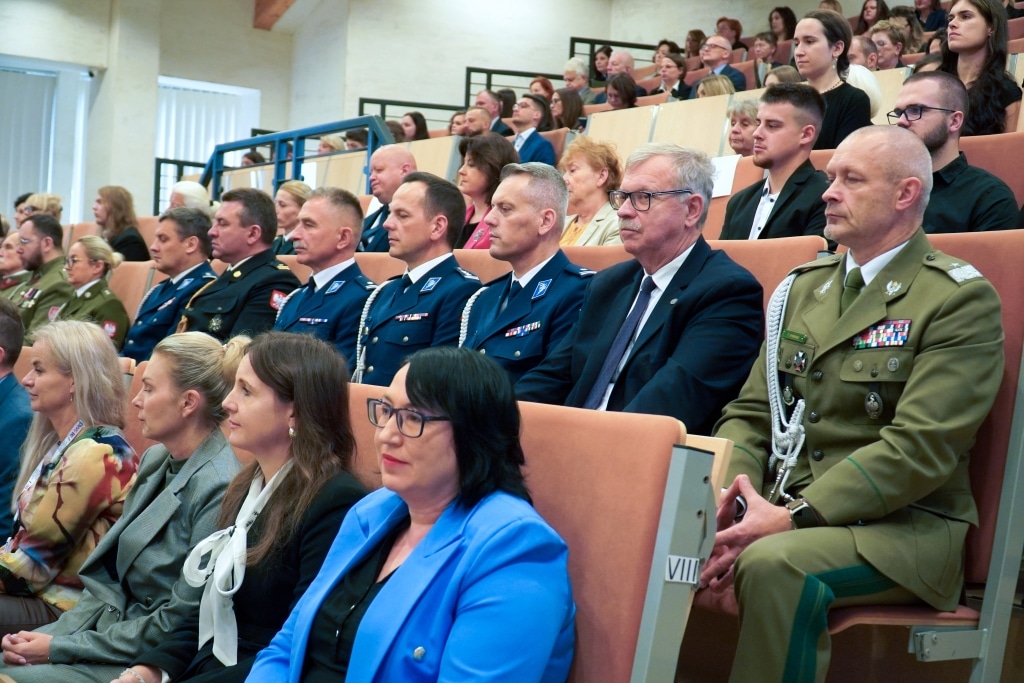 Uroczysta inauguracja roku akademickiego: goście w mundurach i togach siedzą na widowni.