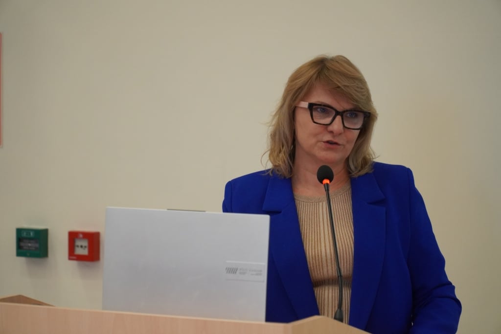 Kobieta w okularach przemawia na IX Konferencji Naukowej