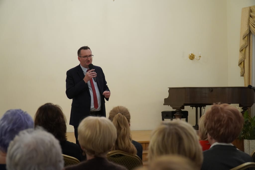 Mężczyzna w garniturze przemawia na inauguracji roku akademickiego Akademii Trzeciego Wieku.