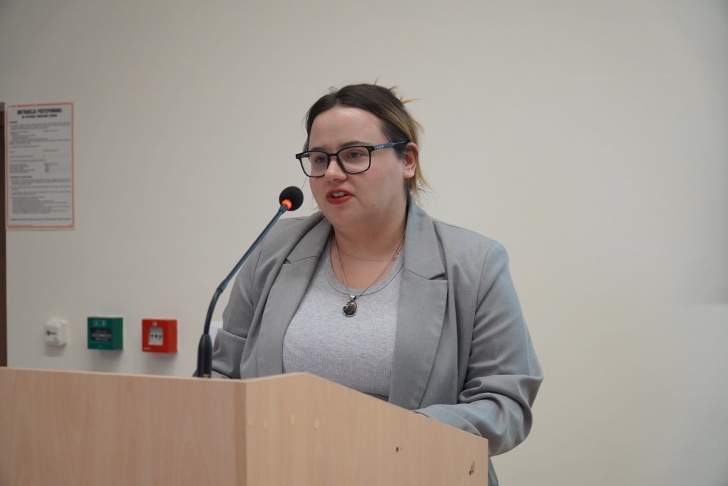 Kobieta w okularach i marynarce przemawia przy mównicy na konferencji Bezpieczeństwo Informacyjne.