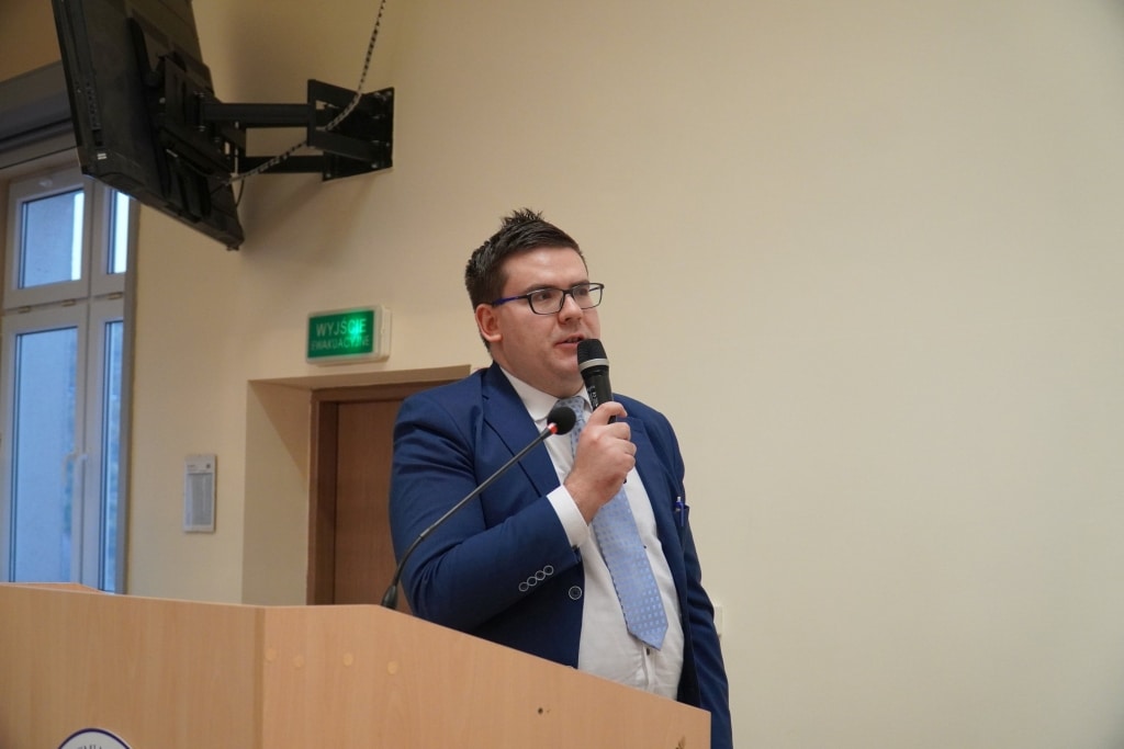 Mężczyzna w garniturze z mikrofonem przemawia na konferencji „Bezpieczeństwo Informacyjne w Zarządzaniu Kryzysowym”