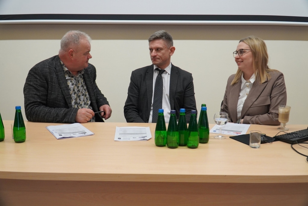 Trzy osoby siedzą przy stole podczas konferencji naukowej Bezpieczeństwo Informacyjne w Zarządzaniu Kryzysowym.