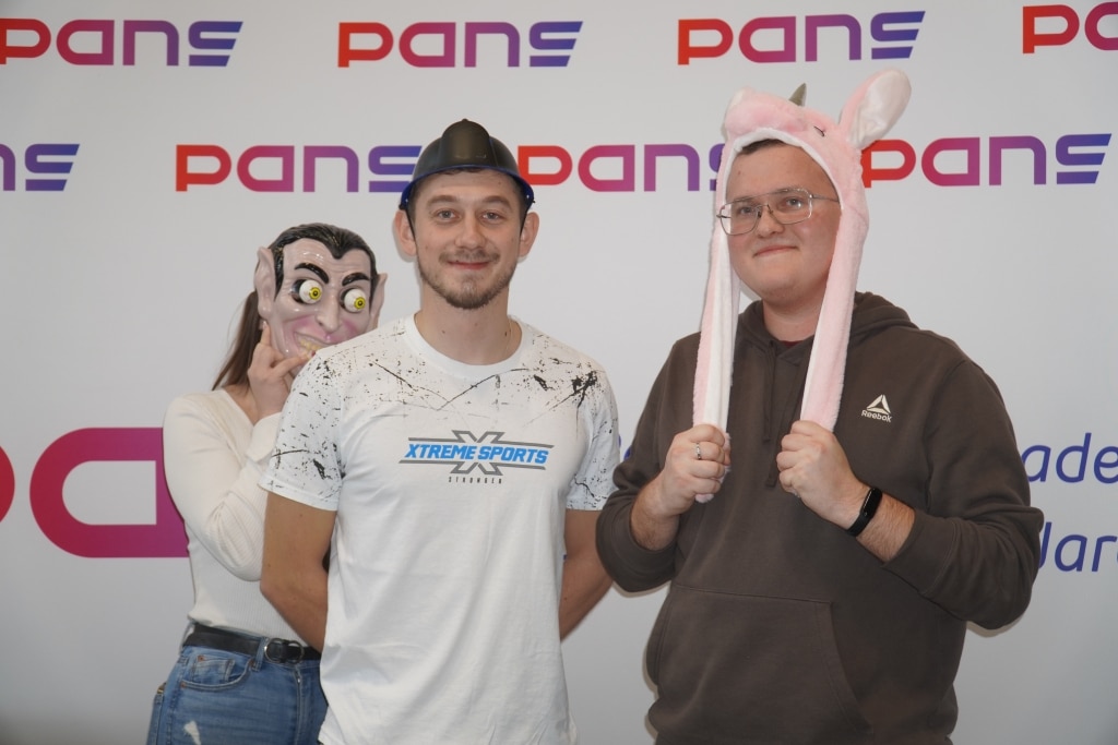 Studenci w śmiesznych nakryciach głowy i maskach na tle logo PANS