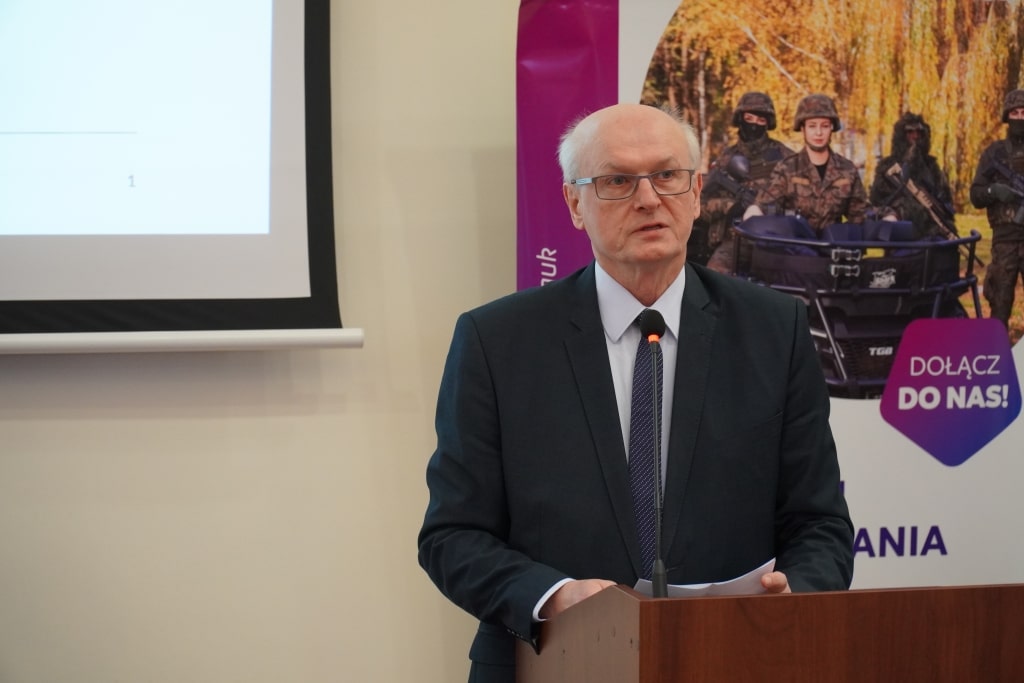 Mężczyzna w garniturze przemawia na tle prezentacji o KSeF