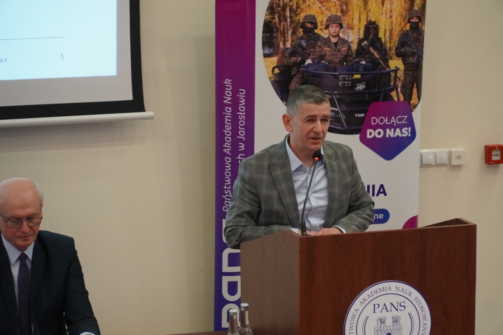 Mężczyzna przemawia na tle baneru Państwowej Akademii Nauk Stosowanych w Jarosławiu