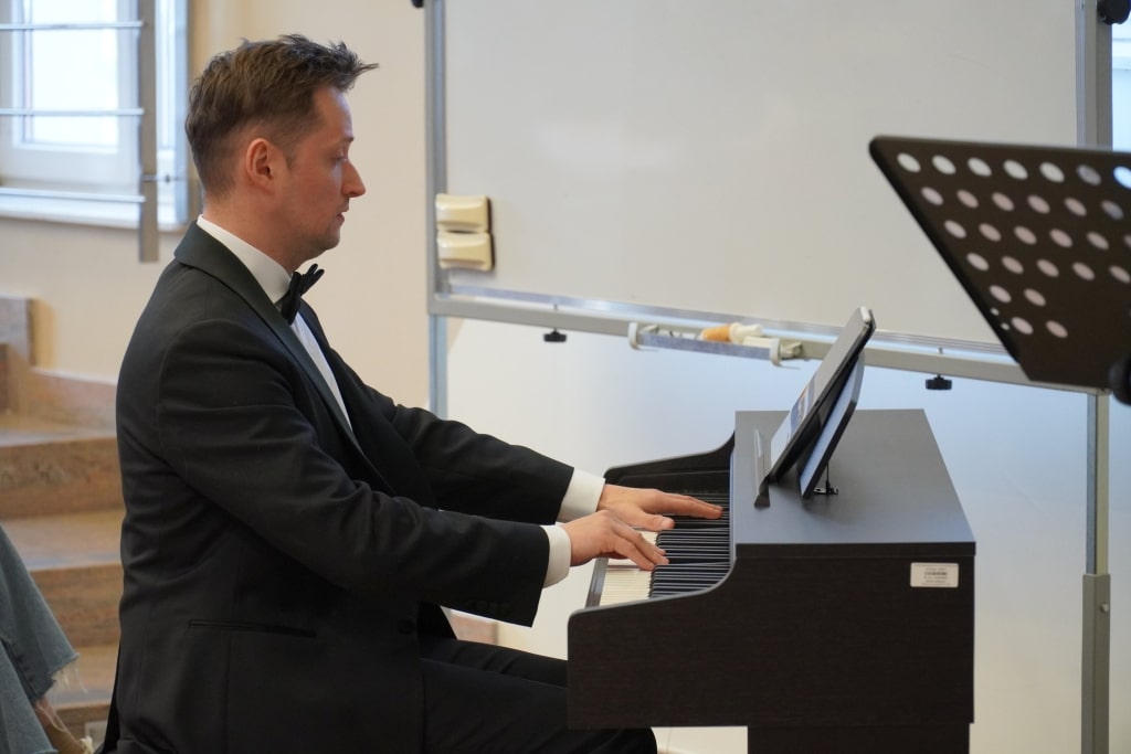 Pianista w czarnym smokingu gra na fortepianie podczas konferencji naukowej WH