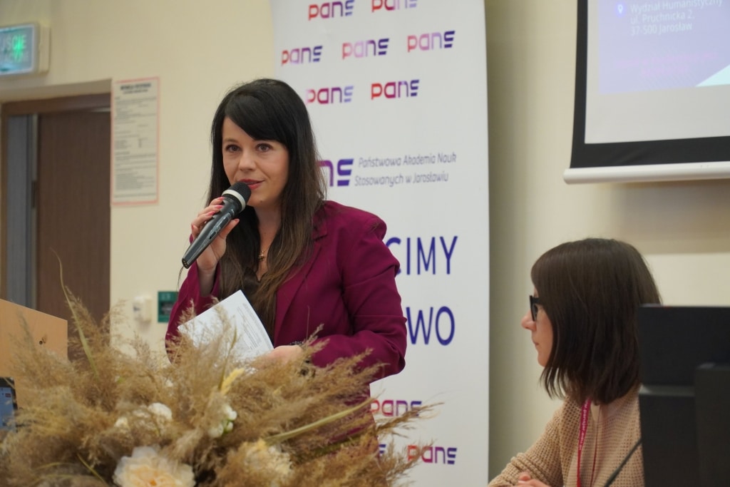Konferencja naukowa WH: prelegentka przemawia na tle logo
