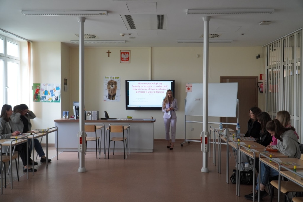Konferencja psychologiczna: prelegentka przed tablicą, uczestnicy siedzą