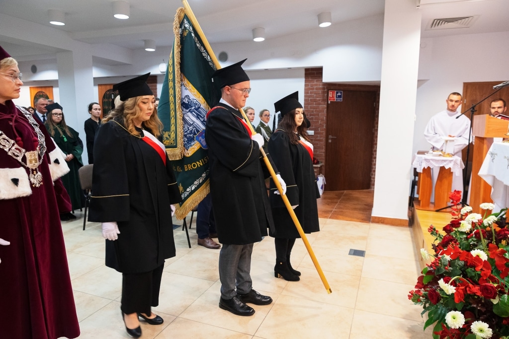 Uroczysta inauguracja roku akademickiego: studenci w togach i biretach niosą sztandar.
