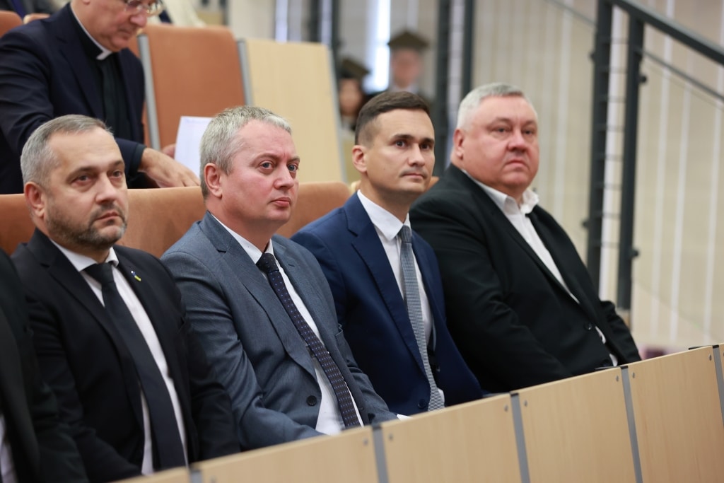 Mężczyźni w garniturach siedzą w sali wykładowej podczas inauguracji roku akademickiego.