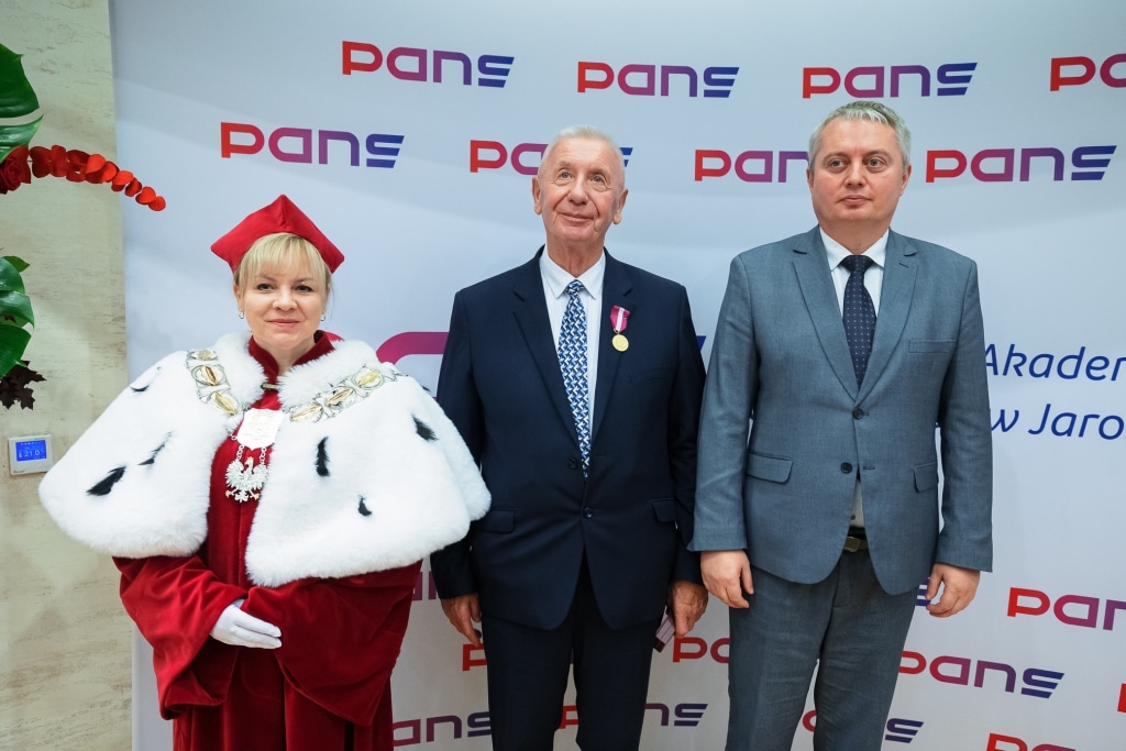 Inauguracja Roku Akademickiego: Trzy osoby w togach i garniturach przed logo PANS