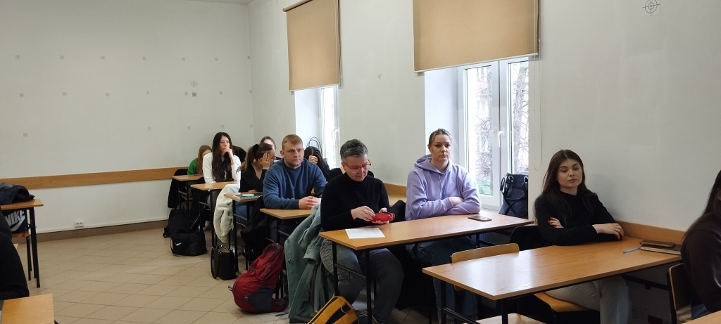 Uczestnicy warsztatów z kompetencji menadżerskich siedzą przy ławkach w sali wykładowej.