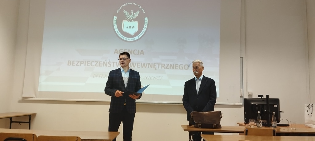 Spotkanie z Delegaturą ABW: dwaj mężczyźni stoją przed ekranem z logo Agencji Bezpieczeństwa Wewnętrznego.