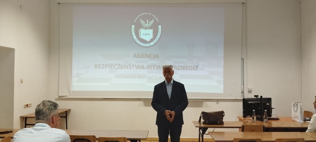 Spotkanie z delegaturą ABW: mężczyzna stoi przed ekranem z logo Agencji Bezpieczeństwa Wewnętrznego.