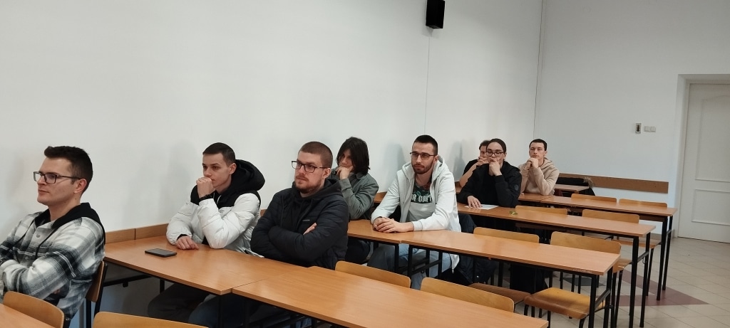 Uczestnicy spotkania z Dowództwem Komponentu Wojsk Obrony Cyberprzestrzeni siedzą przy ławkach.