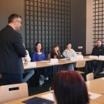 Warsztaty inteligencji emocjonalnej w biznesie: mężczyzna przemawia do grupy osób siedzących przy stołach.