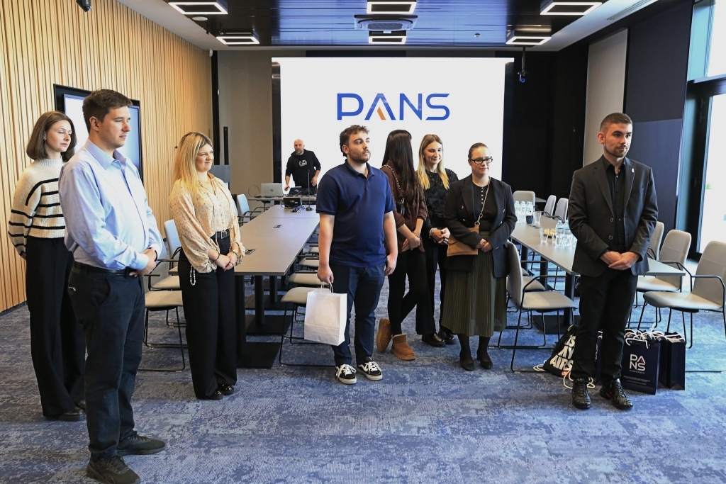 Grupa osób stoi przed logo PANS w sali konferencyjnej