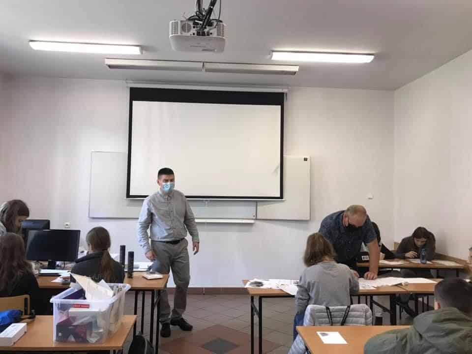 Grupa ludzi w sali lekcyjnej z projektorem i tablicą