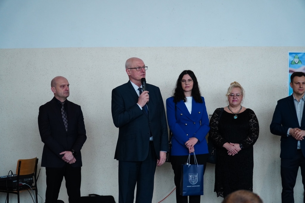 Mężczyzna z mikrofonem przemawia na gali wolontariatu, obok stoją osoby